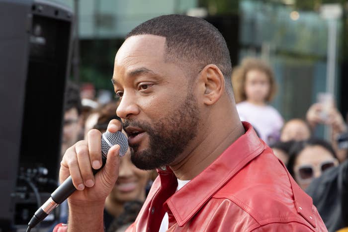 Will Smith successful a stylish casual overgarment speaks into a microphone astatine an outdoor event