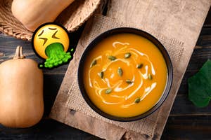 Bowl of butternut squash soup with seeds next to butternut squash. Vomiting emoji added for comic effect