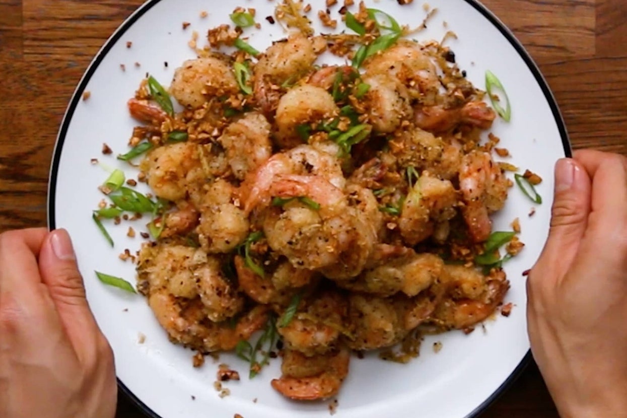 A plate of garlic shrimp garnished with chopped green onions, held on a wooden table