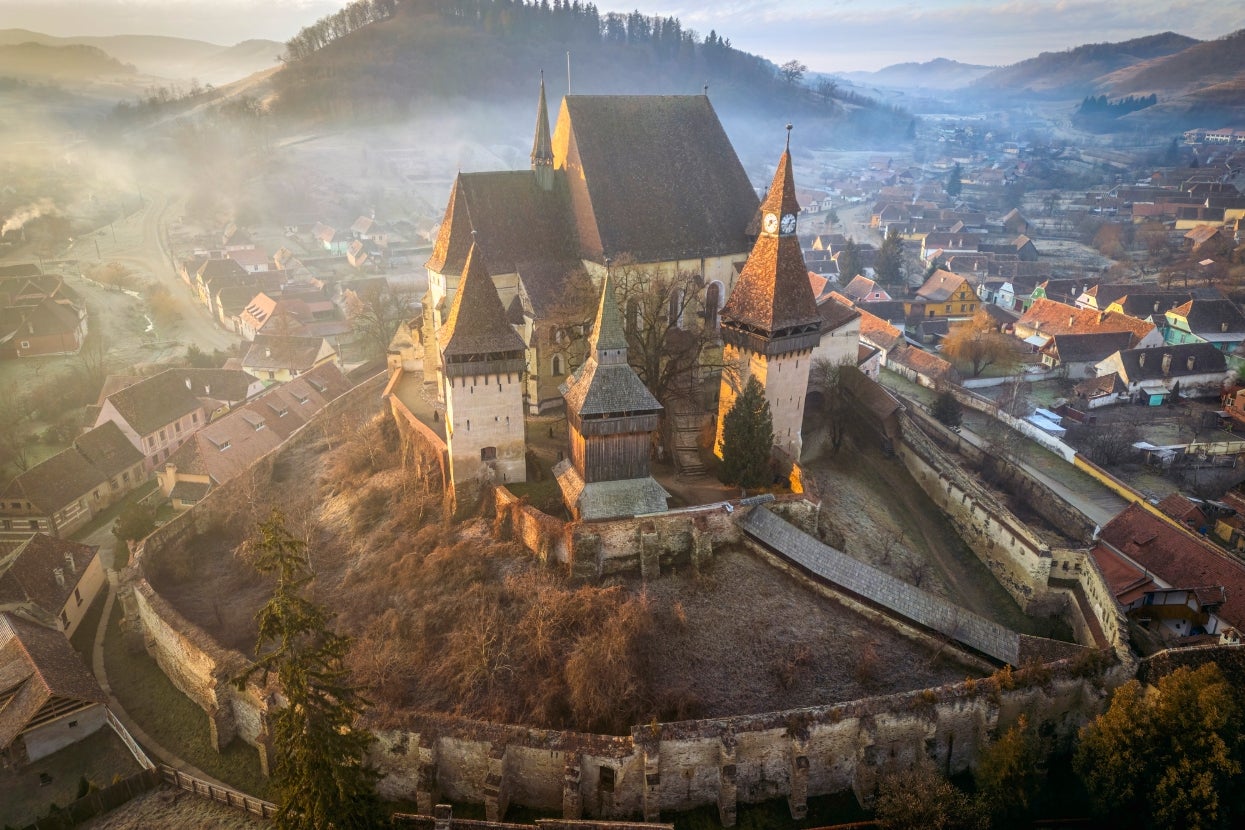 Medieval castle with fortified walls atop a hill, surrounded by a foggy village and distant hills, creating a misty, serene landscape