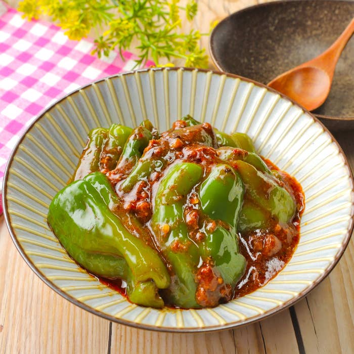 ピーマンの肉詰め料理が平皿に盛られている。背景に木製のテーブルが見える。