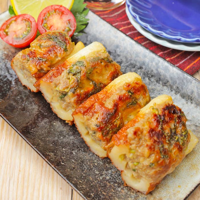 皿に並べられた焼きチーズが乗った肉料理。トマトとレモンが添えられている。