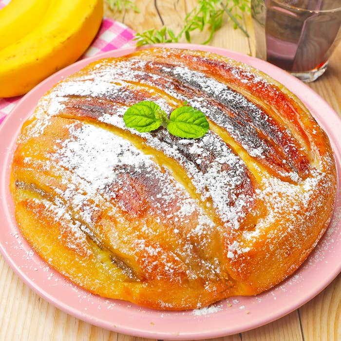 テーブルに置かれた粉砂糖がかかった丸いパンケーキ。バナナと緑の葉が飾られている。