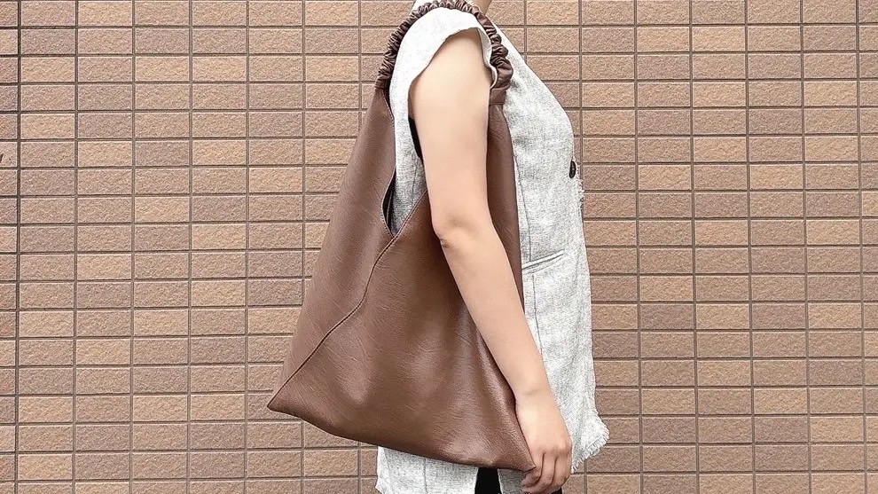 Person in a sleeveless top holding a large, slouchy brown handbag against a brick-patterned wall