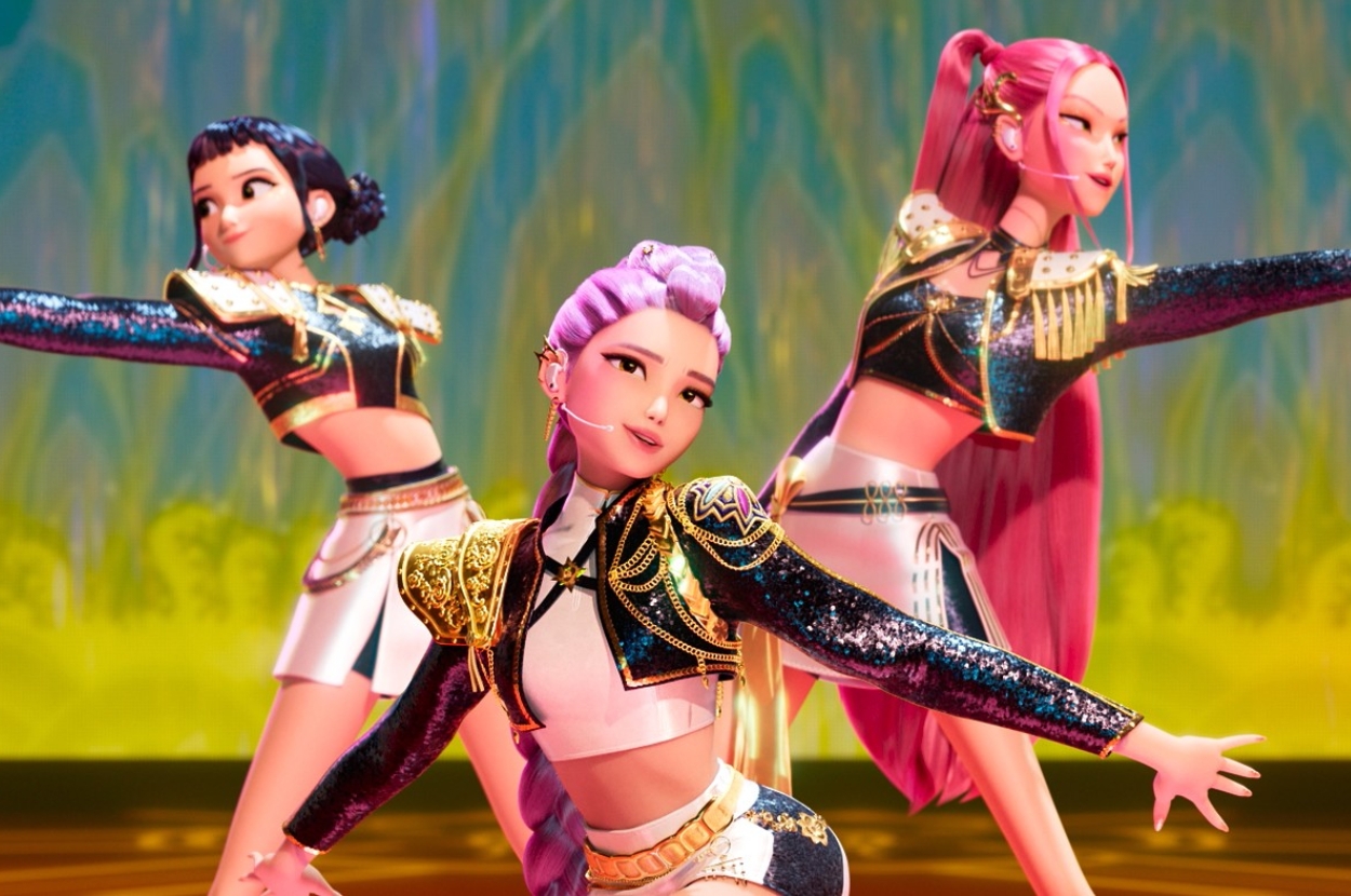 Zoey, Rumi, and Mira perform a dance routine wearing glittery, futuristic outfits with intricate patterns on a stage with a colorful backdrop