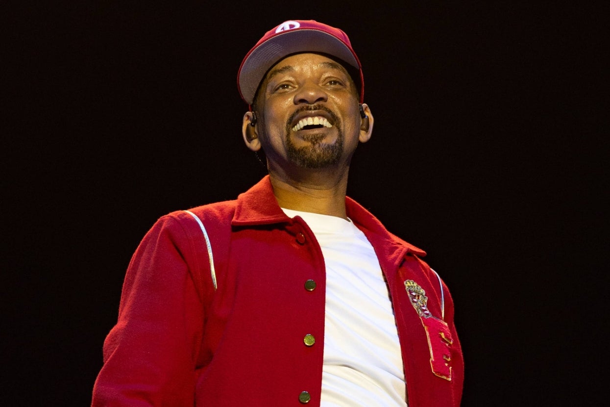 Person in a casual white shirt and red jacket with a logo, smiling brightly on stage