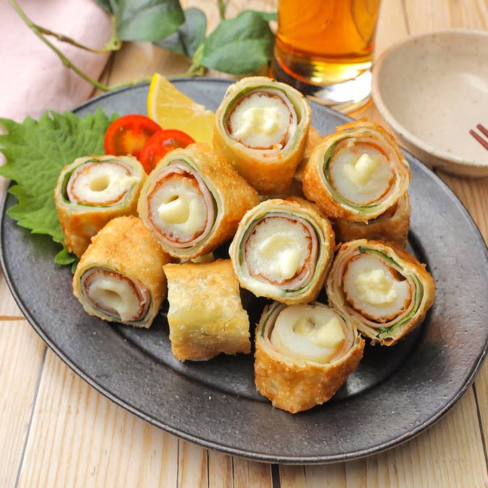 プレートに盛られた巻き寿司風フライ。中にチーズと野菜が見える。後ろにはソース皿と飲み物。