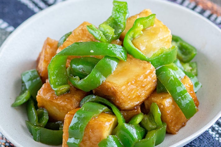 白い皿に盛られたピーマンと揚げ豆腐の料理。伝統的な布の上に置かれている。