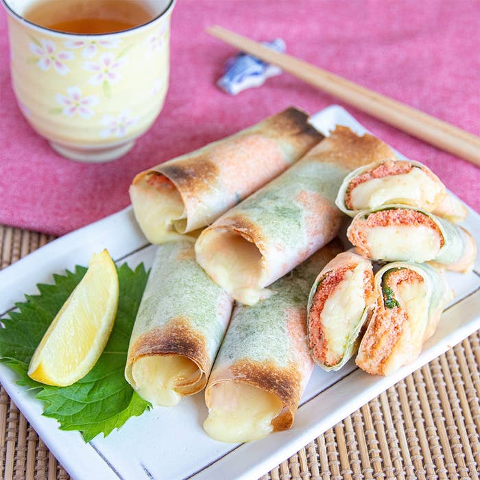 お皿に盛られたチーズ入り春巻きとレモンスライス、横にシソの葉、奥に置かれた飲み物と箸。