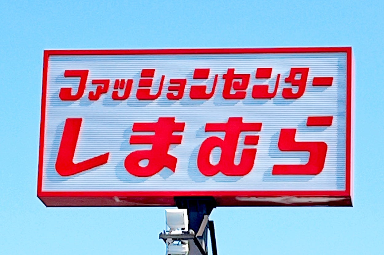 Sign with Japanese text that reads "Fashion Center Shimamura" against a clear sky background