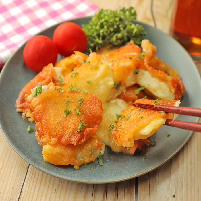 おいしそうな料理が皿に盛られ、トマトとハーブ添えで箸でつままれている様子。