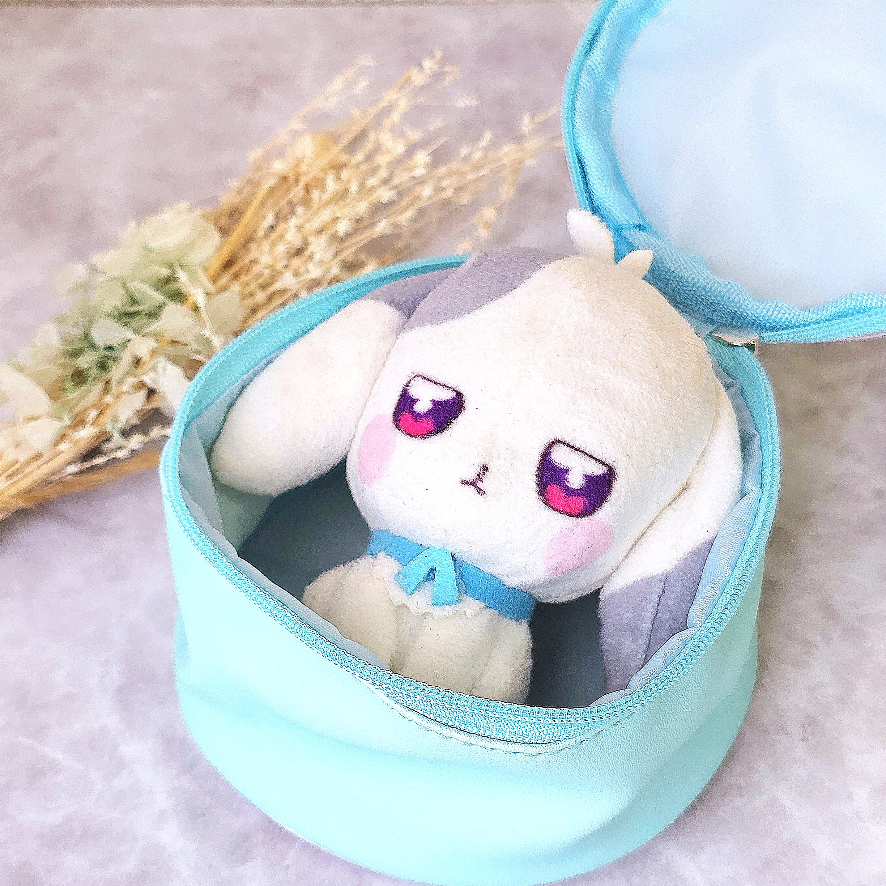青いポーチに入った、耳の長いぬいぐるみ。そばに乾燥した草花が置かれている。