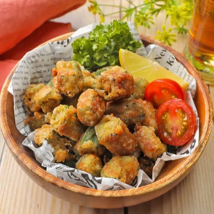 揚げた野菜の盛り合わせが木製のボウルに入っており、添え物としてレモン、トマト、レタスが添えられています。