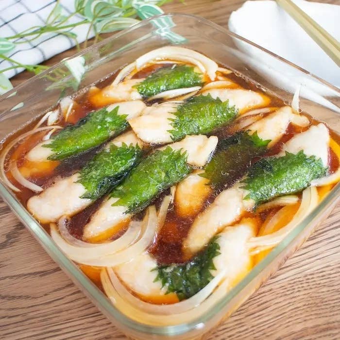 ガラス皿に盛られた魚の切り身と葉がトッピングされた料理。ソースが絡んでいる。