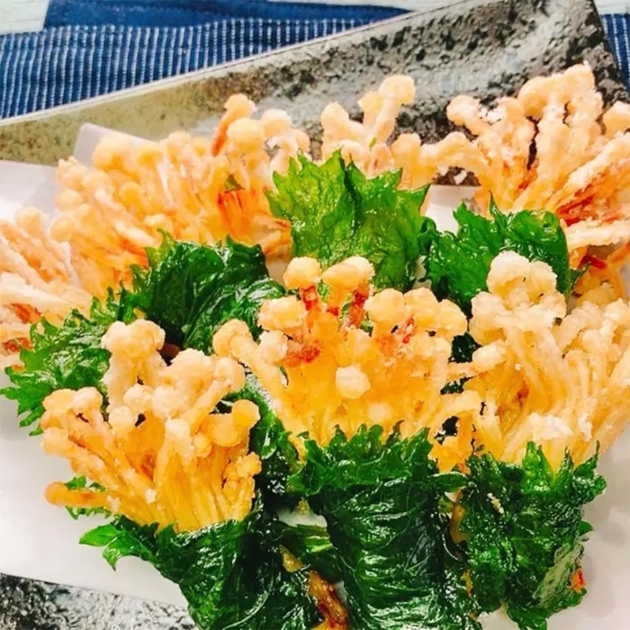 エノキタケと葉野菜の天ぷらが皿に盛られている。カリッとした食感が伝わる盛り付けです。