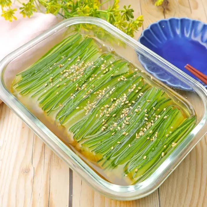 透明な保存容器に、上にゴマが載ったネギの層がある料理が並ぶ。隣に青い皿。