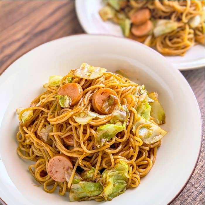 皿に盛られた焼きそば。キャベツと魚肉ソーセージが入っている。助手近くにもう一皿。