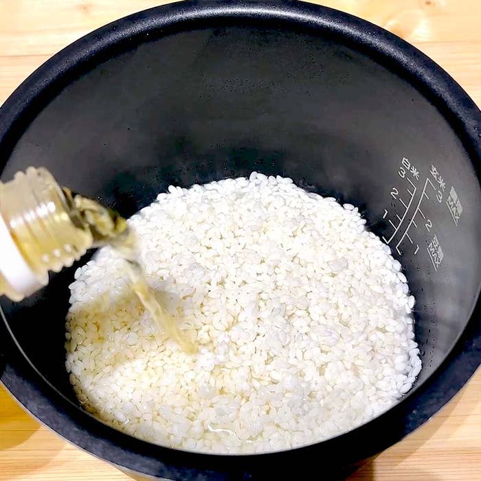 炊飯釜に入れられた米に液体が注がれている。調理の準備風景。