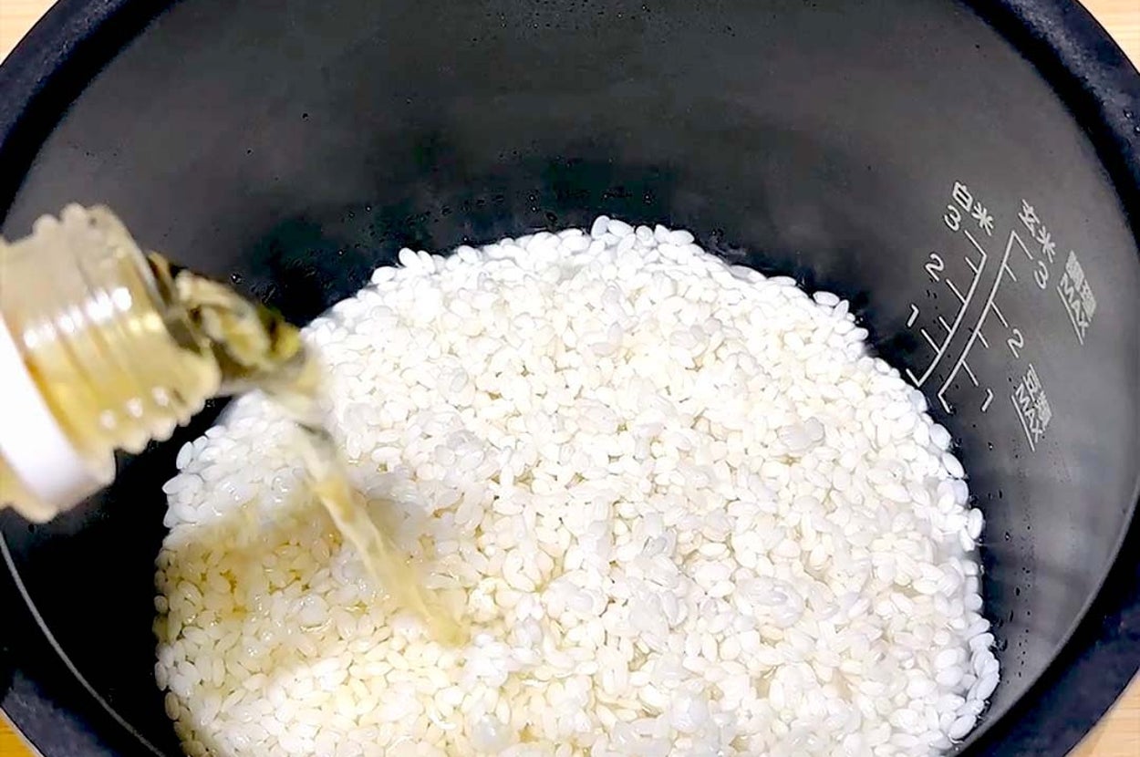 炊飯器の中にある生米に透明な液体が注がれる様子。