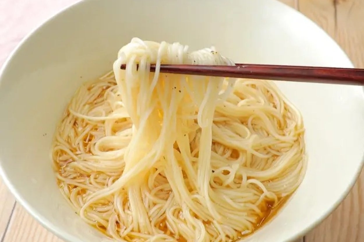 箸で持ち上げられたそうめんが白いボウルに入っています。シンプルなソースがかかっています。