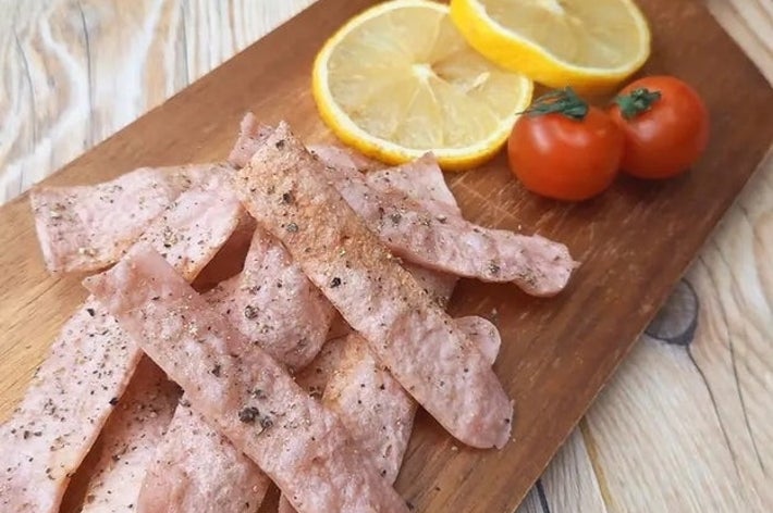 レモンとミニトマトが添えられた木製ボードに並ぶ薄い肉の切れ端。
