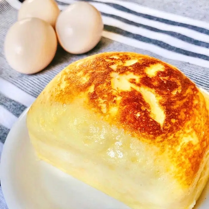 皿に焼きたてのふわふわ卵パンが置かれ、背景に3つの卵が写っています。