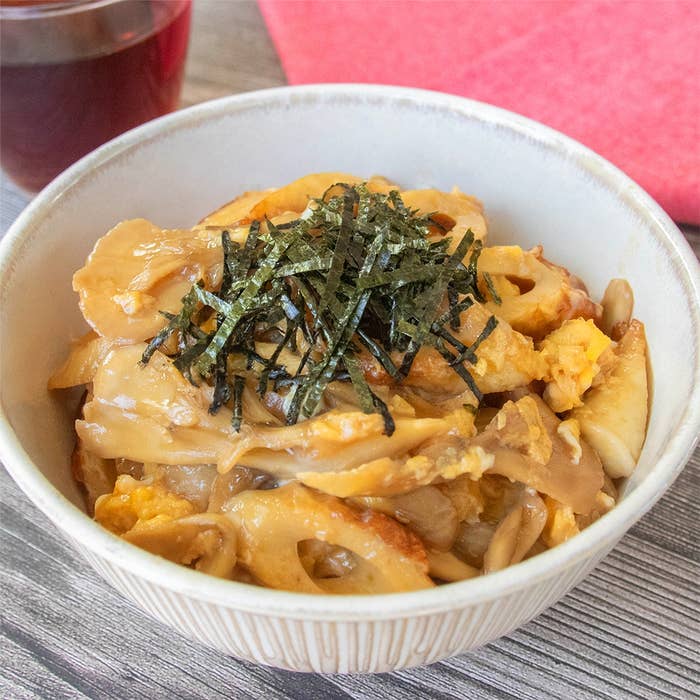 どんぶりに盛られたちくわとまいたけの卵とじ丼。刻みのりが上にのり、背景には赤布が見える。