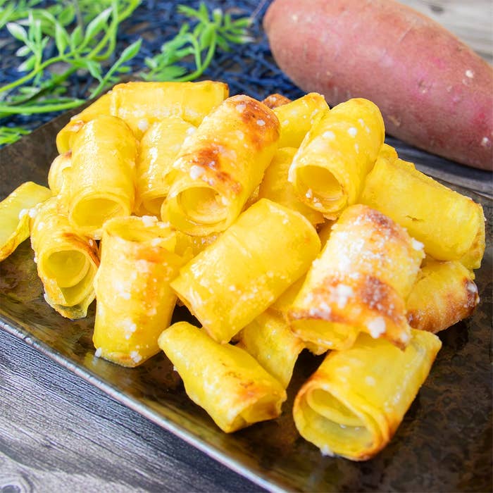 さつまいもに、バターと粉砂糖で味付けされたカリカリのおやつが黒い皿に盛られています。背景にさつまいもが置いてあります。