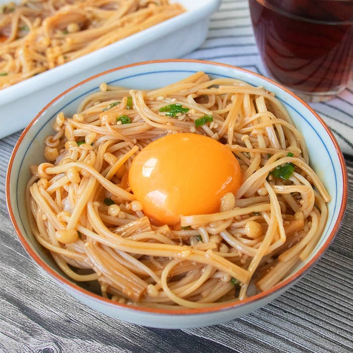 韓国風の味付けのえのきに卵の黄身がのった料理が茶わんに盛られている。隣には飲み物が置かれている。