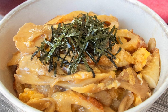 どんぶりに盛られたちくわとまいたけの卵とじ丼。刻みのりが上にのり、背景には赤布が見える。