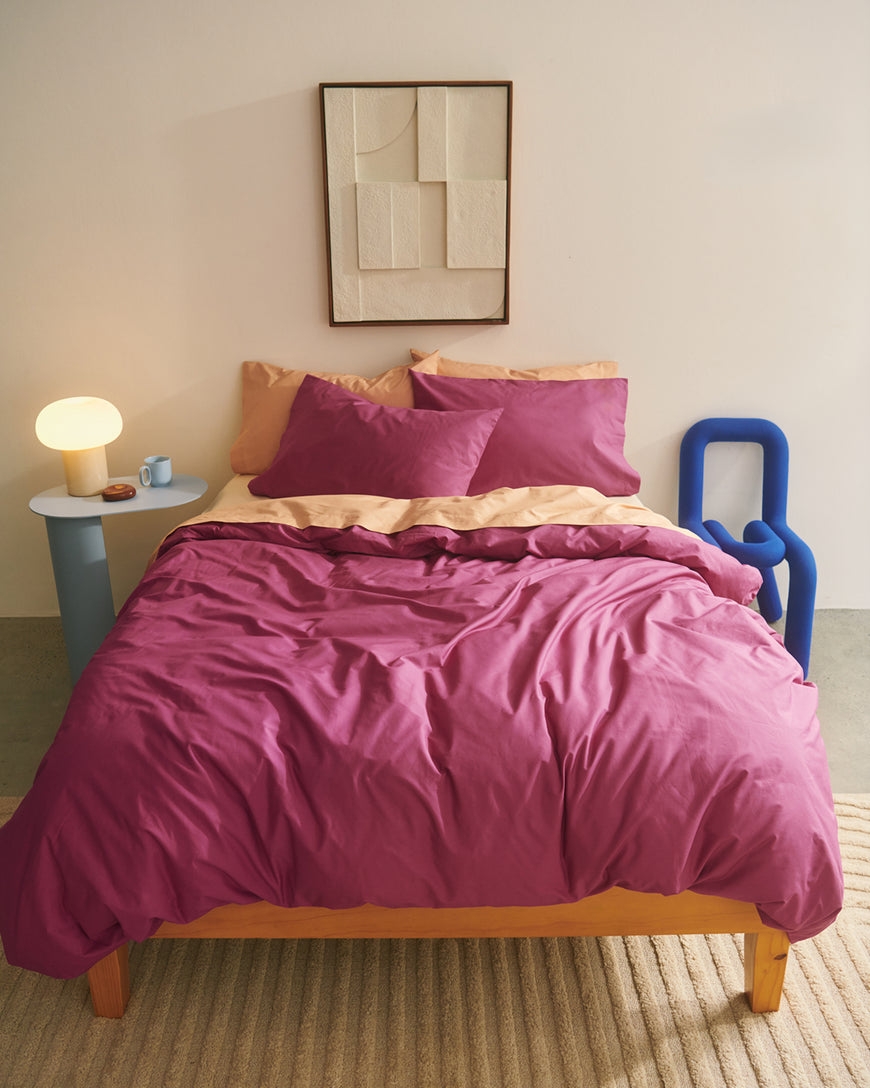 Cozy bedroom scene with a neatly made bed featuring magenta and beige linens, a modern art piece above, and a stylish lamp on a side table