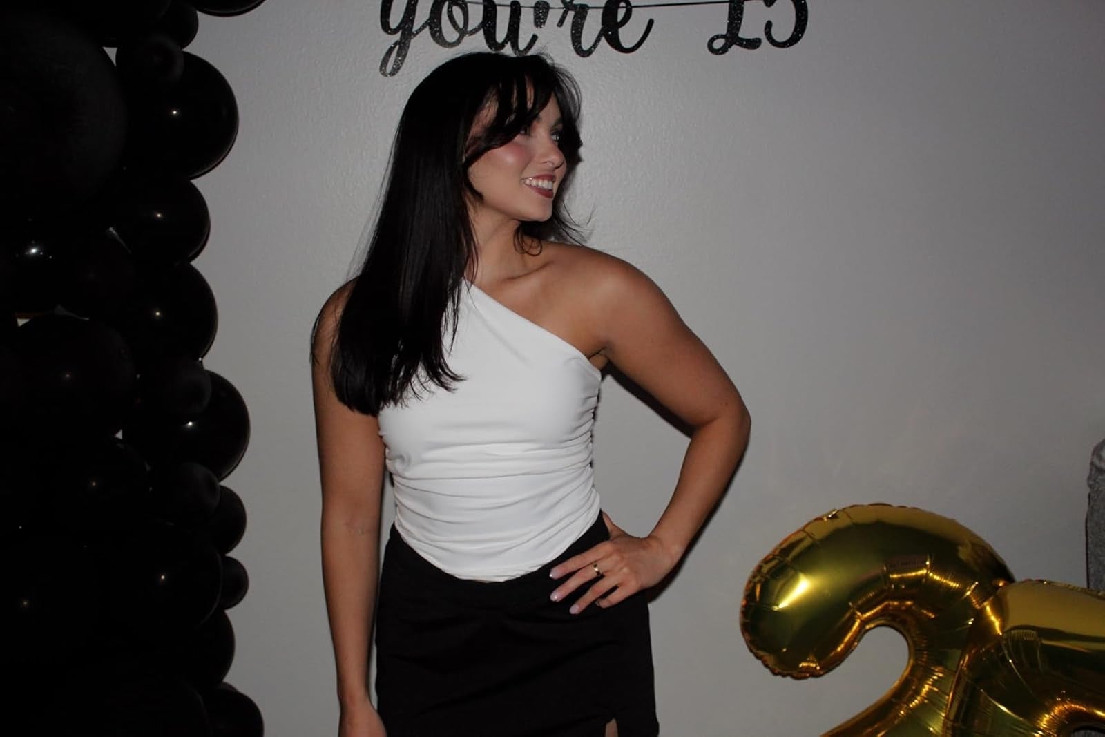 Person in a one-shoulder top and skirt at a party with large gold number balloons