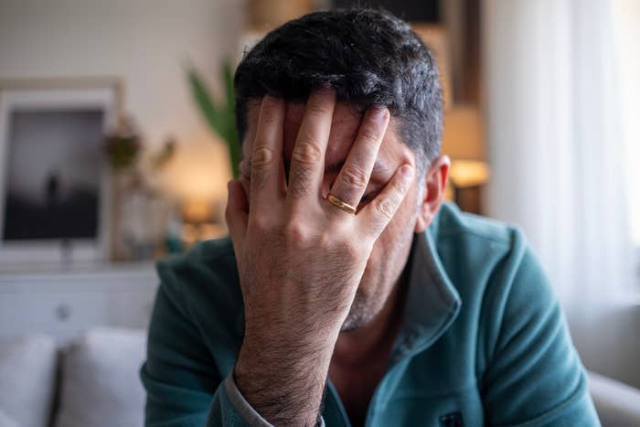 Person with manus covering face, showing a golden wedding ringing connected a finger, successful a motion suggestive of vexation oregon exhaustion