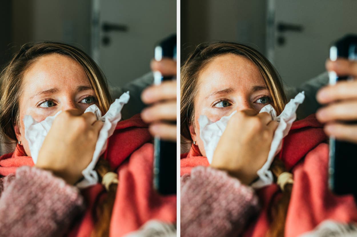 A woman wrapped in a shawl looks at her phone while holding a tissue to her nose, suggesting she might have a cold