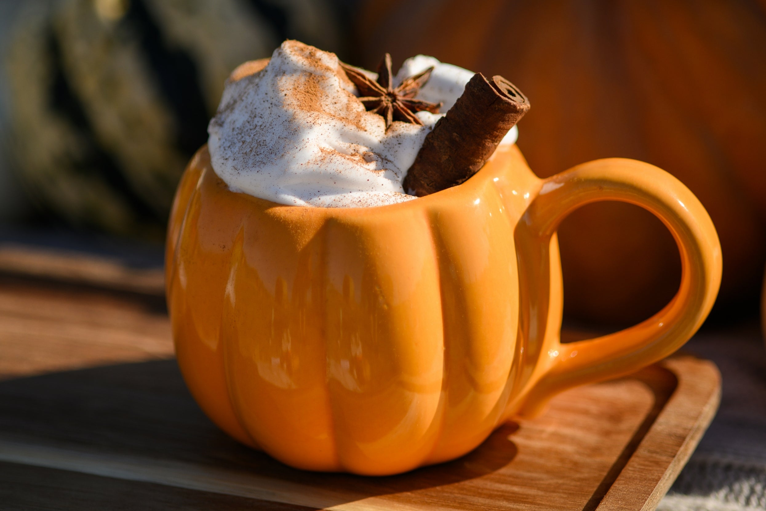 A pumpkin-shaped mug filled with whipped cream, cinnamon, and a star anise, placed on a wooden tray