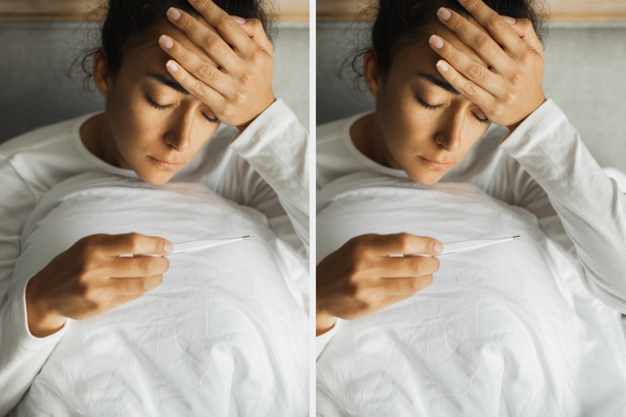 Person in a white shirt holding forehead with one hand and checking a thermometer with the other, appearing concerned