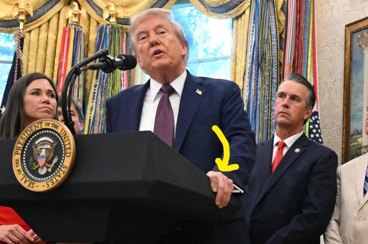 A man in a suit speaks at a podium with the presidential seal, surrounded by others in a formal setting