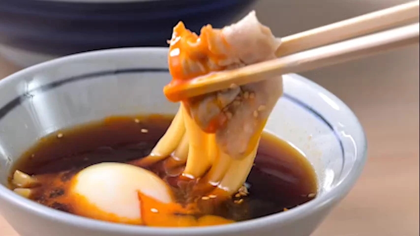 「旨辛 豚つけ汁うどん」を持ち上げている画像/「丸亀製麺」のプレスリリースより