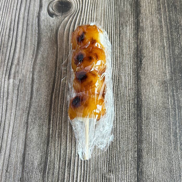 ラップで包まれたみたらし団子が木製テーブルの上に置かれています。