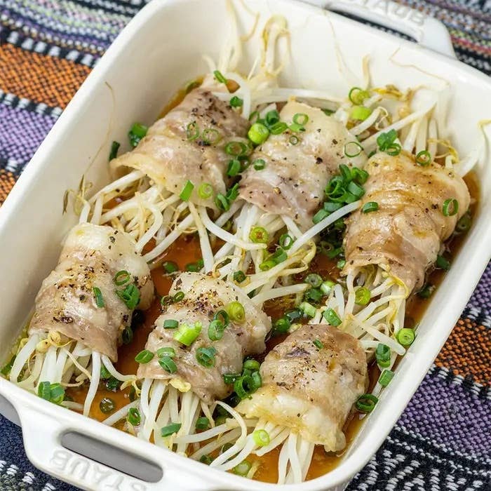 料理された豆もやしを巻いた豚肉のロール、上に刻んだネギが添えられたオーブン皿。