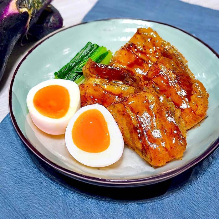 半熟卵と照り焼き風の茄子の料理が皿に盛られている。隣に緑の葉野菜が添えられている。
