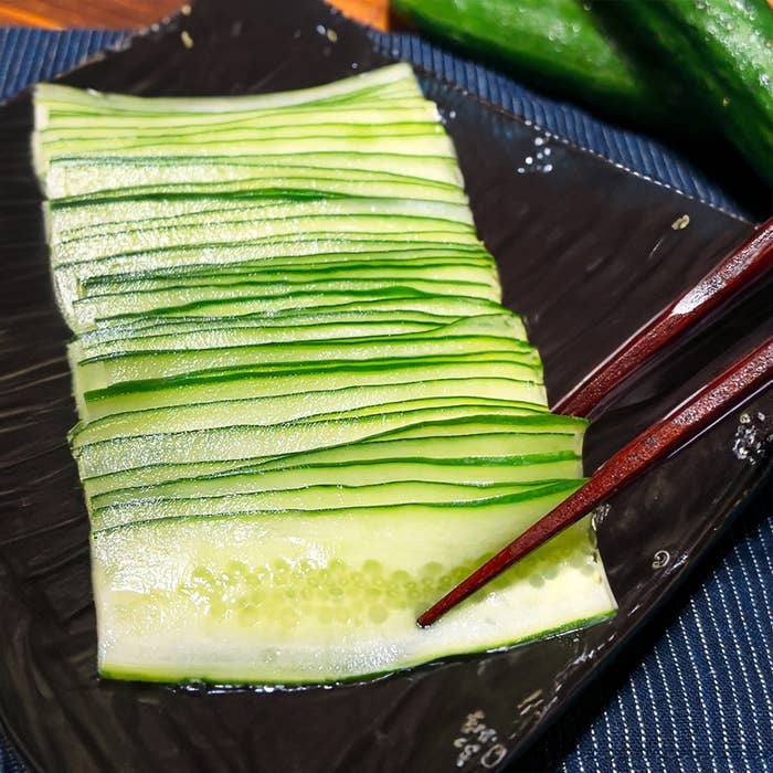 薄くスライスされたきゅうりが黒い皿に整然と並べられ、横に箸があります。