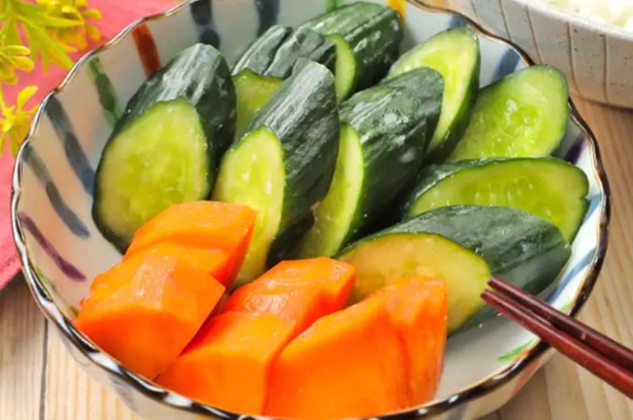 きゅうりとにんじんの漬物が小鉢に盛られている。背景に白いご飯と植物の装飾あり。