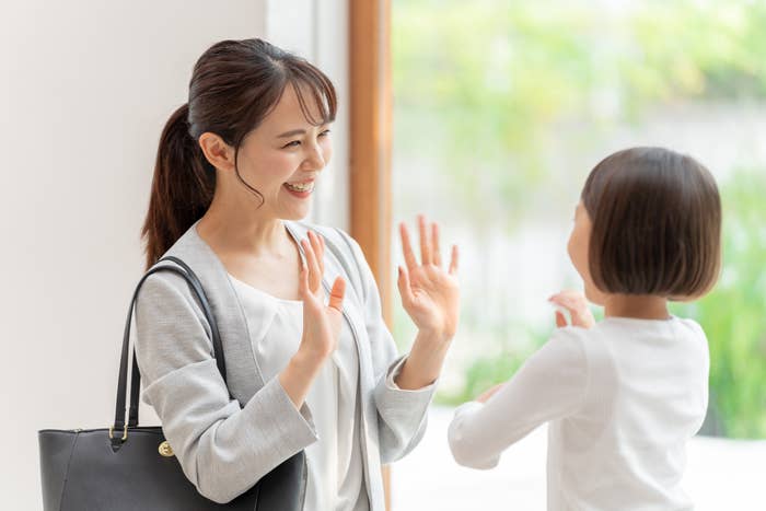 女性が窓際で子どもと笑顔で交流しています。ビジネスバッグを持っています。