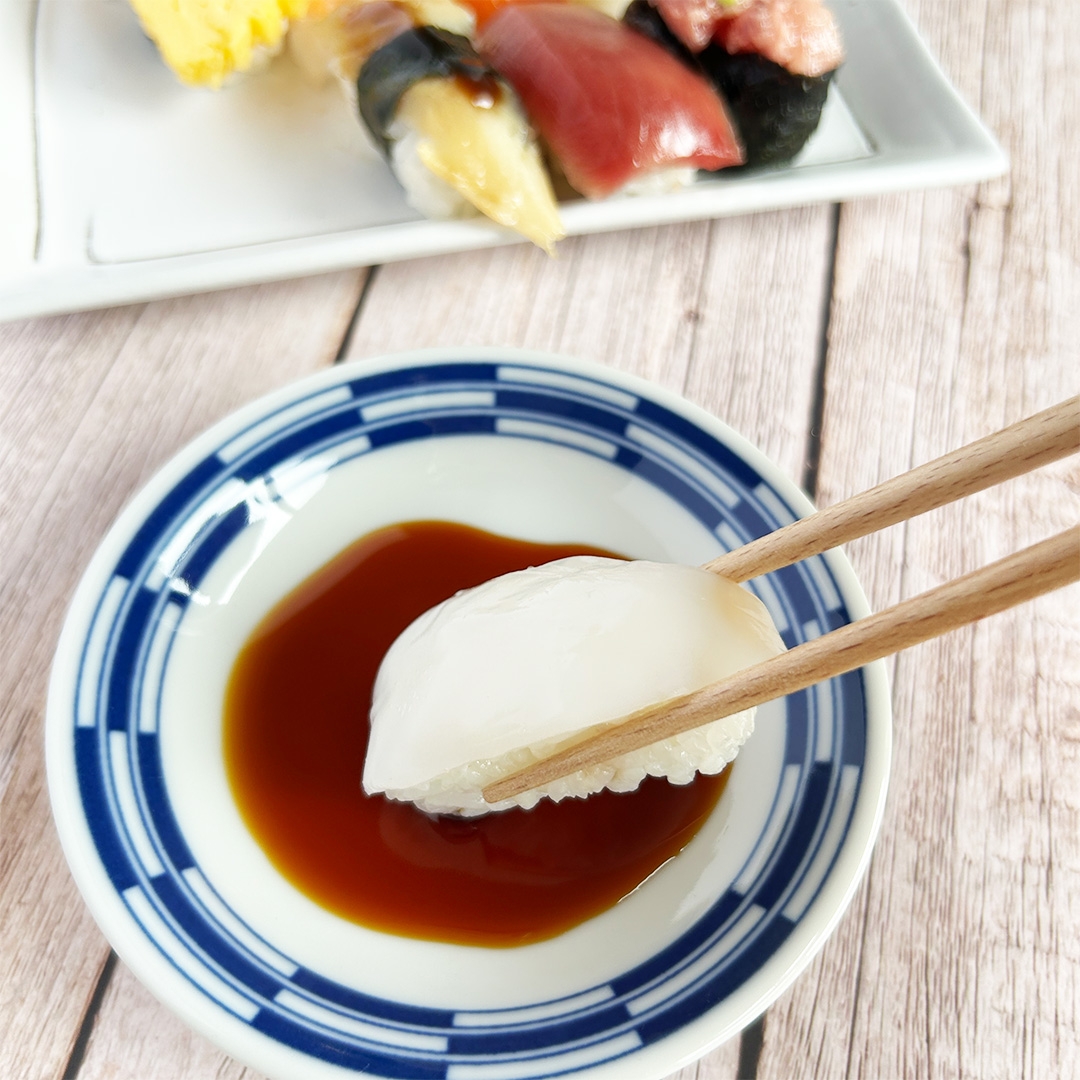 寿司を箸で持ち、醤油につけようとしている様子。手前の皿には醤油が入っている。