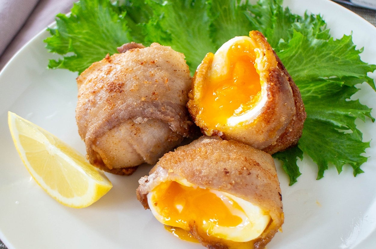 皿に盛られたベーコンで巻いたゆで卵の断面が見える料理。添えられたレタスとレモンの輪切り。