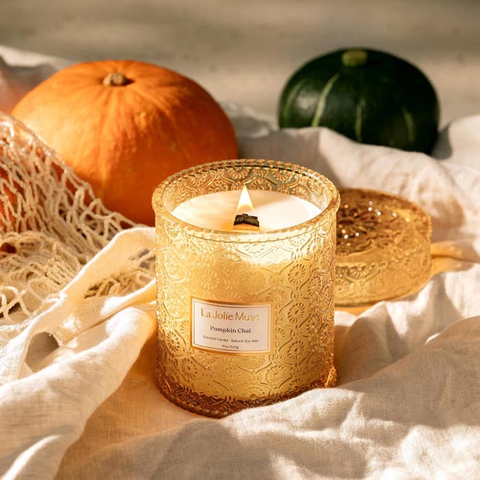 Decorative candle labeled "Pumpkin Chai," surrounded by pumpkins and cozy fabric, suggesting autumn buying vibes