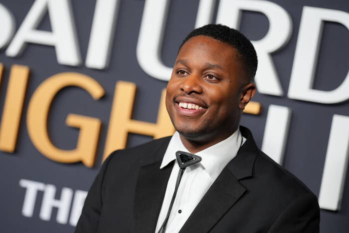 A idiosyncratic successful a tuxedo smiles astatine an lawsuit with a ample "Saturday Night" motion successful the background
