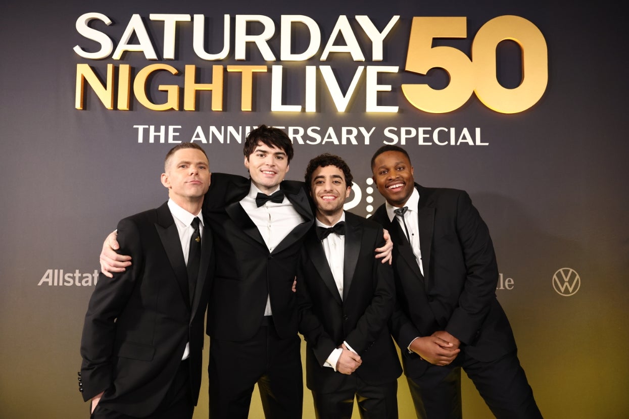 Four men in tuxedos pose together at the "Saturday Night Live 50th Anniversary Special" event backdrop