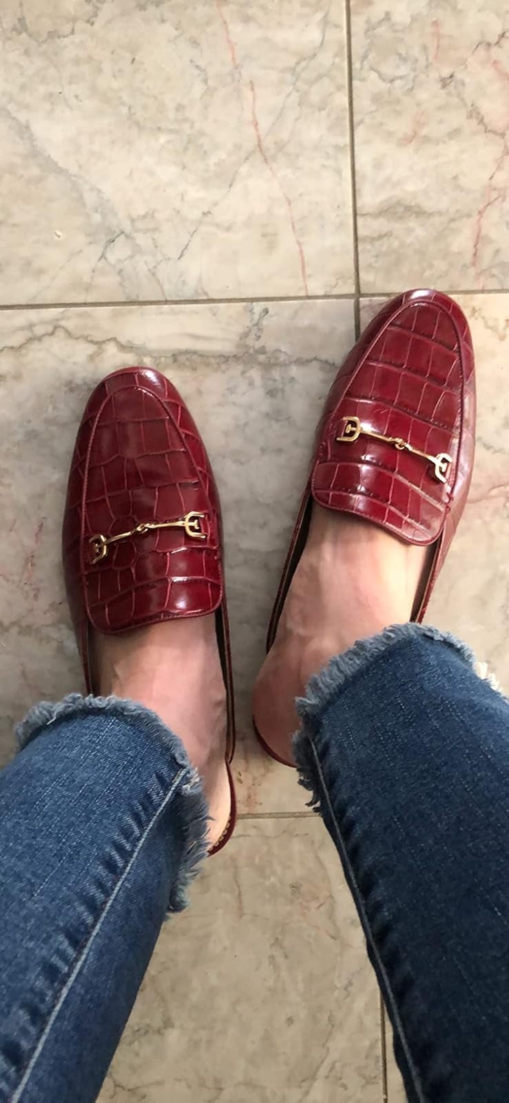 Person wearing jeans and stylish loafers with a croc signifier   and metallic accents connected  a tiled floor